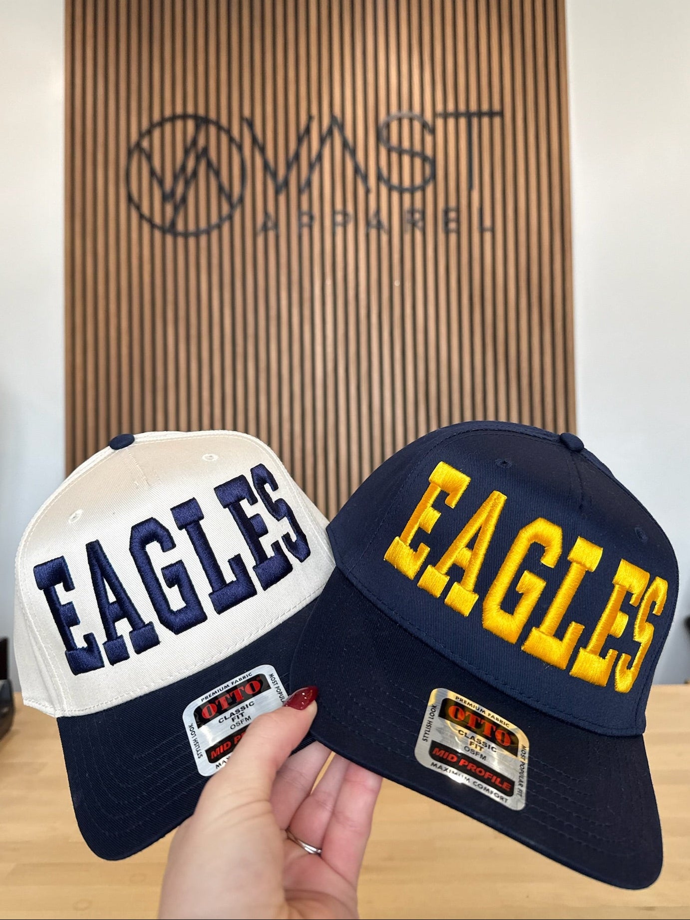 Two Eagles caps held in front of a branded wall.