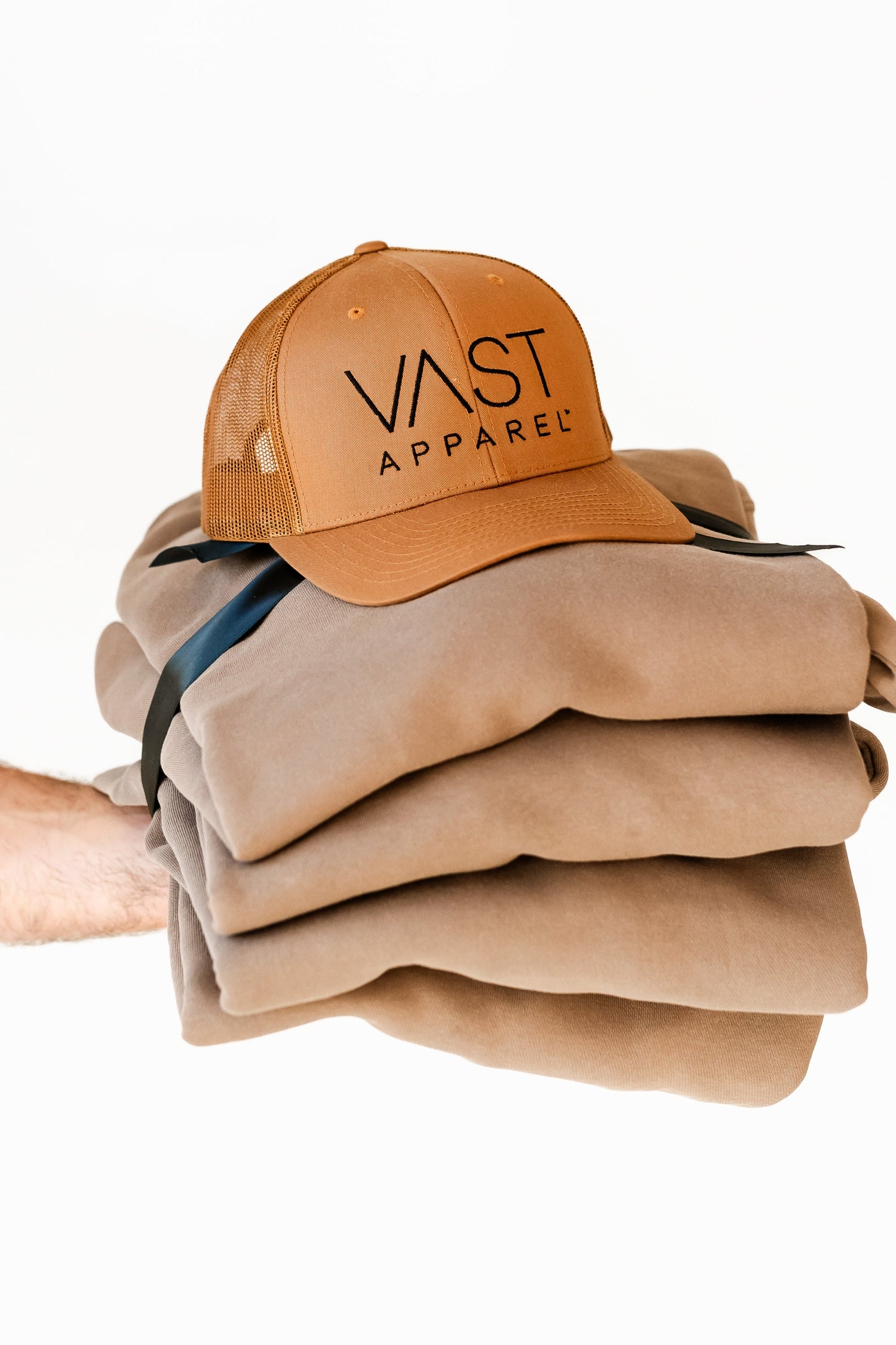 Stack of folded beige clothing with a brown cap labeled 'VAST APPAREL' on a white background